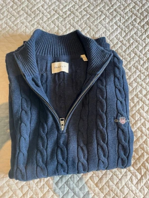 Stickad 1/4 zip från gant - En snygg kabelstickad marinblå tröja från gant med en 1/4 zip. Gjord av bomull fullt ut. Perfekt för kallare dagar. Storlek XL men passar för dig som har L. Den är använd 1-2 ggr och är därför i toppskick