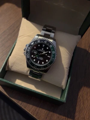 Klocka - Snygg klocka med svart urtavla och tvåfärgad svart och grön vridring. Klockan har en robust länk i rostfritt stål och tydliga indexmarkeringar. Perfekt accessoar för dig som gillar klassisk och exklusiv stil.