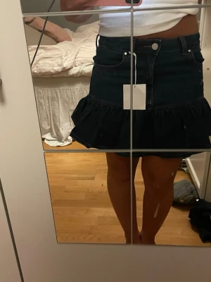 Mörkblå volangkjol i denim - Säljer en snygg mörkblå jeanskjol med volangkant. Helt ny! 