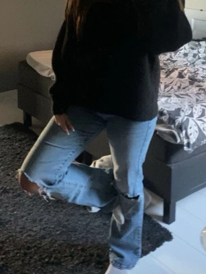 Ljusblå slitna jeans med hål - Säljer ett par högmidjade ljusblå jeans med slitningar och hål vid knäna. Jeansen har klassisk femficksmodell, bälteshällor och dragkedjegylf. Materialet är denim i bomull och passformen är rak med något smalare ben.