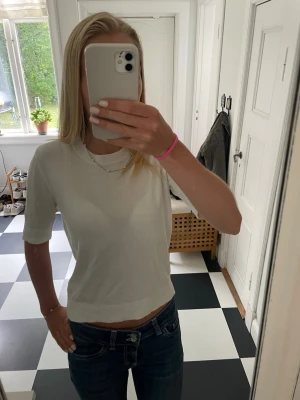 Vit ribbad kortärmad topp - Säljer en enkel och stilren vit topp med ribbad kant i halsen. Toppen har korta ärmar och en croppad passform som passar perfekt till jeans eller kjol. Materialet känns mjukt och stretchigt, troligen bomull eller en bomullsblandning.