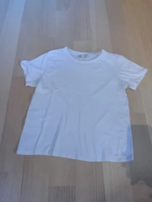 Vit t-shirt från Pull&Bear - Klassisk vit t-shirt från Pull&Bear i mjuk bomull. Enkel design med rund halsringning och korta ärmar, perfekt till alla outfits. Passformen är normal och materialet känns skönt mot huden.