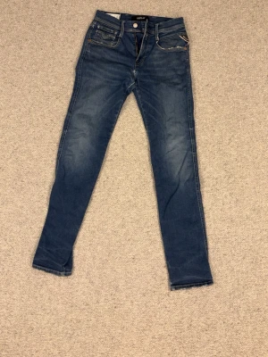Mörkblå slim fit jeans med slitningar - Snygga mörkblå slim fit jeans med lätt slitna detaljer och klassiska fem fickor. Jeansen har guldfärgade sömmar och smal passform som sitter tajt längs benen. Perfekta till en avslappnad laidback look
