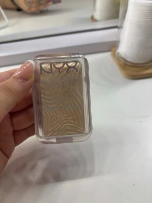 NYX guldig highlighter i dosa - Säljer en guldig highlighter från NYX i en smidig, rektangulär plastdosa med genomskinligt lock. Pudret har ett snyggt vågmönster och ger en riktigt fin glow till huden. Perfekt för att framhäva kindben och andra ansiktsdrag.