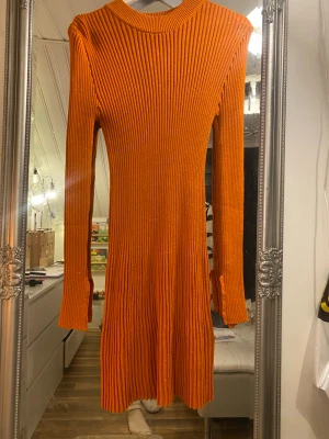 Ribbad orange klänning från Monki - Säljer en ribbad orange klänning från Monki i storlek M. Klänningen har lång ärm, rund halsringning och är stickad i ett mjukt material. Perfekt för dig som vill ha en färgstark och bekväm look.