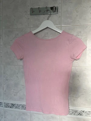 Ljusrosa tight topp med öppen rygg - Söt ljusrosa topp med tight passform och korta ärmar. Toppen har en djup, öppen rygg som ger en snygg detalj. Perfekt att styla med jeans eller kjol. Strechtigt och bekvämt material💓