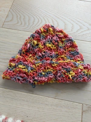 Färgglad handvirkad mössa - Unik mössa i handstickad stil med grov struktur och färger i rosa, gul och blå. Garnet är fluffigt och ger en cool, bohemisk vibe. Perfekt för dig som vill sticka ut och gillar färg. Passar till höst och vinter när du vill hålla dig varm och snygg.