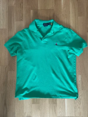 Grön pikétröja med krage - POLO Raulph Lauren - Snygg grön pikétröja med klassisk krage och korta ärmar. Tröjan har en liten broderad detalj på bröstet och är tillverkad i ett mjukt bomullsmaterial. Perfekt för en avslappnad och stilren look.