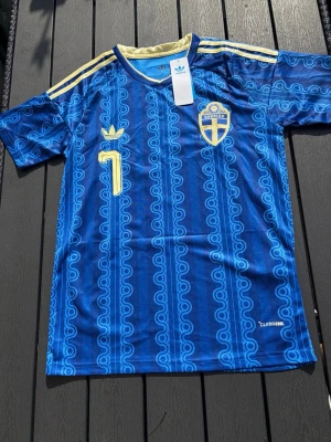 Blå Sverige fotbollströja Adidas - Säljer en blå Sverige fotbollströja från Adidas med gult tryck, nummer 7 och namnet Bergvall på ryggen. Tröjan har gula detaljer, Sveriges landslagsemblem och är tillverkad i lätt och ventilerande ClimaCool-material.