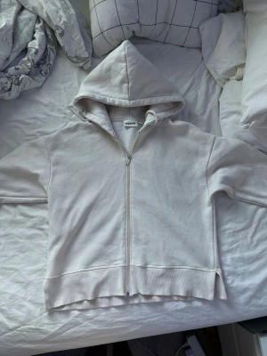 Vit/creme hoodie med dragkedja från Kappahl - Säljer en enkel och stilren vit hoodie från Kappahl. Hoodien har dragkedja framtill, stor huva och ribbade muddar vid ärmslut och nederkant. Tillverkad i mjukt bomullsmaterial och har en avslappnad passform. Perfekt för en chill och casual look.