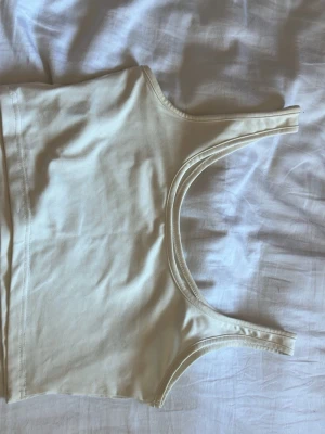 Vit croppad topp från SHEIN - Säljer en enkel och stilren vit croppad topp från SHEIN i storlek XS. Toppen är ärmlös med breda axelband och har en mjuk och stretchig känsla, perfekt till sommaren. Passar till allt och är lätt att matcha med andra plagg.