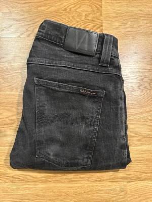 Svarta Nudie jeans w32 L32 - Hej, Säljer ett par svarta nudie jeans med en femficksmodell och diskret logga på bakfickan. Jeansen är riktigt snygga och är tillverkade i slitstark denim matrial med snygg look. Perfekta för dig som gillar en stilren och avslappnad vibe. Obs dem är inte söndertvättade dem är så i modellen! 