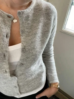Grå stickad kofta  - Mysig grå kofta i en mjuk, stickad ullblandning. Croppad modell med rund halsringning och knäppning framtill. Perfekt att styla med jeans eller kjol för en avslappnad look.