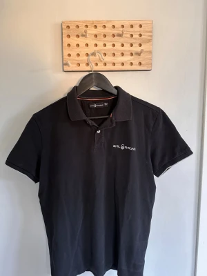 Svart piké från Sail Racing - Klassisk svart pikétröja från Sail Racing, perfekt för en fet outfit. 