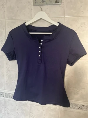 Mörkblå t-shirt med knappar - En cool mörkblå t-shirt med korta ärmar och knappdetaljer framtill. T-shirten har en tajt passform med mycket skönt material. Tröjan är aldrig använd!💕