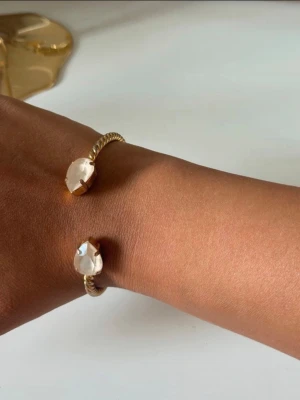 Guldigt armband Caroline Svedbom - Superfint öppet cuff-armband med Swarovski-kristaller i en mjuk, matt ton snarare än helt klar/glansig finish. One size och justerbart.  Guldpläterad metall. En del av pläteringen har släppt på vissa partier, vilket syns på bilderna, men helhetsintrycket är fortfarande fint.  Elegant statement-armband som är snyggt både ensamt och tillsammans med andra armband.  Stil: crystal bracelet, Swarovski crystal, open cuff, adjustable bracelet, gold plated, statement jewelry, romantic, feminine, boho chi