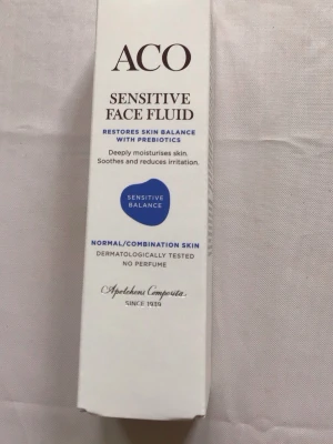ACO Sensitive Face Fluid foundation - ACO Sensitive Face Fluid är en foundation för normal/kombinerad hud. Den är parfymfri, dermatologiskt testad och innehåller prebiotika, hyaluronsyra och panthenol som återfuktar och lugnar huden. Produkten kommer i en vit förpackning och innehåller 50 ml.