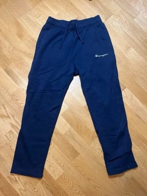 Mörkblå mjukisbyxor Champion - Säljer dessa mörkblåa mjukisbyxor från Champion med broderad logga på vänster ben. Byxorna har dragsko i midjan, resår och två sidofickor. Tillverkade i mjukt bomullsmaterial som är skönt att ha på sig. Vid frågor, extra bilder eller liknande är det bara att kontakta mig!