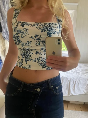 Vit blommig linnetopp från Cider - Supersnygg vit linnetopp från Cider med blått blommigt mönster. Toppen har breda axelband, draperad framsida och är ärmlös. Perfekt för sommarens alla outfits och ger en fräsch och trendig look.