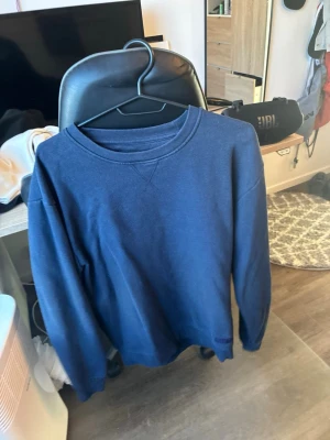 Mörkblå sweatshirt från Sams Basic - En enkel och stilren mörkblå sweatshirt från Sams Basic i storlek M. Tröjan har rund halsringning och ribbade muddar vid ärmslut och nederkant. Perfekt för en avslappnad look och lätt att matcha med jeans eller joggers.