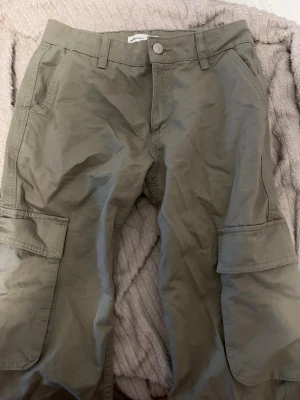 Gröna cargobyxor  - Snygga gröna cargobyxor med stora sidofickor och bakficka med lock. Byxorna har raka stora ben, bälteshällor och är gjorda i ett slitstarkt bomullstyg. Perfekta för en avslappnad look.