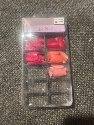 Mixade press-on naglar i rosa toner - Säljer ett set press-on naglar i olika rosa och korallfärger. Naglarna har en elegant, spetsig form och kommer i flera nyanser från ljusrosa till mörkrosa och orange. Perfekt för dig som vill ha snygga naglar snabbt och enkelt.