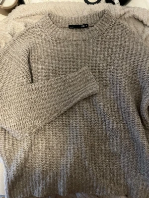 Beige/grå stickad tröja  - Mysig beige/grå stickad tröja från lager157 med grovstickad struktur och rund hals. Tröjan har långa ärmar och ribbade muddar vid ärmslut och nederkant. Perfekt för lager på lager under kyliga dagar.