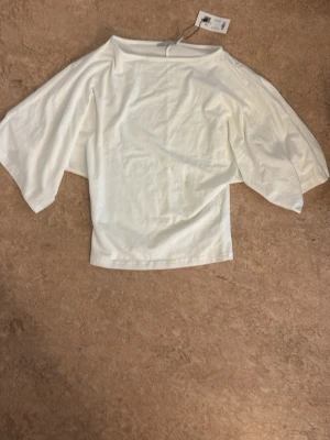 Vit topp med vida ärmar - Snygg vit topp med vida, nästan fladdriga ärmar och rak passform. Tillverkad i mjukt material som känns skönt mot huden. Perfekt att styla med jeans eller kjol för en clean look.