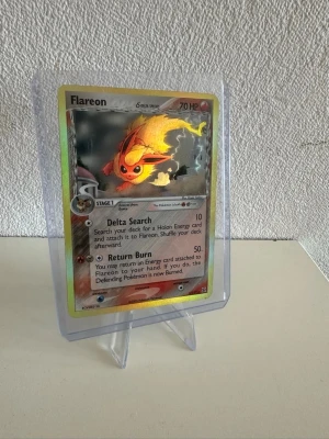 Pokémonkort Flareon Delta Species - Säljer ett holografiskt Pokémonkort med Flareon från Delta Species-serien. Kortet har en färgstark design med Flareon i eldiga toner och silverglänsande detaljer. Text och effekter på engelska. Perfekt för samlare eller Pokémonfans.