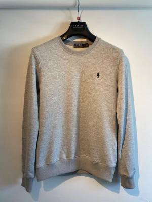 Ralph Lauren tröja, strl S - Säljer en riktigt fin tröja från Ralph Lauren i grå. Mycket fint skick utan fläckar eller hål. Storlek: S  Självklart äkta och skickas inom 24h efter köp! Hör av er vid minsta fråga.