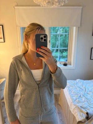 Grå mjukisdress med dragkedja - Säljer en grå mjukisdress med hoodie och dragkedja framtill. Tröjan har fickor. Perfekt för chill dagar hemma. Materialet är mjukt och bekvämt. 
