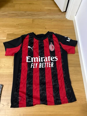 AC Milan matchtröja Puma röd/svart - Säljer en officiell AC Milan matchtröja från Puma i rött och svart med klassiska vertikala ränder. Tröjan har klubbmärke och Puma-logga på bröstet samt sponsortryck framtill. Tillverkad i lätt och ventilerande material, perfekt för fotbollsträning.