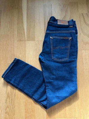 Nudie Jeans - W32 L30 - Snygga mörkblå jeans från Nudie Jeans med klassisk och stilren modell. Fina detaljer med kontrastsömmar och den ikoniska Nudie-loggan på bakfickan.  📏 Storlek: W32 L30 🎨 Färg: Mörkblå ✨ Skick: Mycket fint skick 👖 Klassisk rak/slim passform