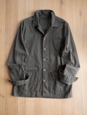 Olivgrön overshirt med fickor - Stilren olivgrön overshirt i bomull med klassisk krage och knäppning framtill. Tre stora utanpåfickor ger en avslappnad look. Perfekt lager-på-lager-plagg för dig som gillar enkel och funktionell stil.
