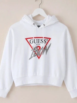Croppad hoodie Guess y2k glitter  - Säljer en vit hoodie från Guess med det klassiska röda triangelloggan och texten 'ICON' i silverglitter framtill. Hoodien har huva med dragsko och ribbade muddar. Perfekt för dig som gillar streetstyle och vill sticka ut lite extra.