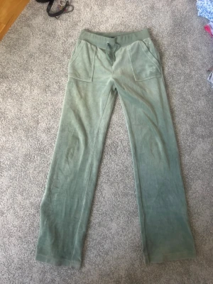 Gröna Juicy mjukisbyxor i velour - Snygga gröna äkta juicy mjukisbyxor i mjuk velour med raka ben och bred resår i midjan. Byxorna har stora fickor fram och bak, bakfickorna har lock och silverfärgade knappar. Köpte för 1200kr.