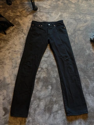 Levi's 501 - Snygga svarta jeans från Levi's med rak passform och klassisk femficksdesign. Jeansen har metallknappar och nitar samt bälteshällor. Materialet är slitstarkt denim i bomull. Perfekta för en clean och stilren look.