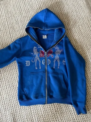 Rhinestone hoodie - Sällsynt blå hoodie med huva och dragkedja framtill från Le Dos. Framsidan har ett tryck av rhinestones. Dragkedjan kan även gå upp hela vägen över huvudet. 