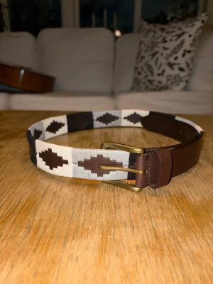 Svart och vitt mönstrat skärp - Helt nytt och inplastat svart-vitt färgat broderat bälte i färgerna: svart, grå och vit. Extremt fräscht bälte som ger din outfit en sista detalj. Finns 5 olika storlekar att välja mellan: 80-110 cm. Hör av er vid minsta fundering!