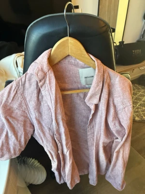 Rosa linneskjorta från Only & Sons - Säljer en snygg rosa skjorta från Only & Sons i linnematerial. Skjortan har klassisk krage, långa ärmar och knappar framtill. Perfekt för dig som gillar en avslappnad men ändå stilren look.