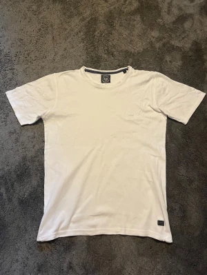 Vit basic t-shirt i bomull - En enkel vit t-shirt med rund hals och korta ärmar. Tillverkad i mjuk bomull och har en lite större passform än S. Perfekt till jeans eller shorts.
