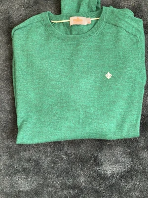 Grön stickad tröja från Morris  - Snygg grön stickad tröja med rund hals och ett litet vitt emblem på bröstet. Tröjan har långa ärmar och ribbade muddar vid ärmslut och nederkant. Perfekt för dig som gillar enkel men stilren design.