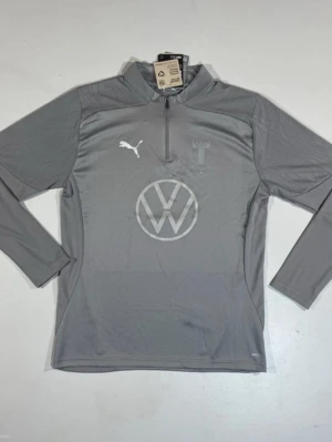 Grå Malmö FF träningströja Puma - Snygg grå långärmad träningströja från Puma med Malmö FF-logga och Volkswagen-tryck på bröstet. Tröjan har halv dragkedja framtill och är tillverkad i ett lätt, tekniskt material som andas. Perfekt för fotbollsträning eller gymmet. Passar M också fast lite tightare. Använd 2 gånger max. 