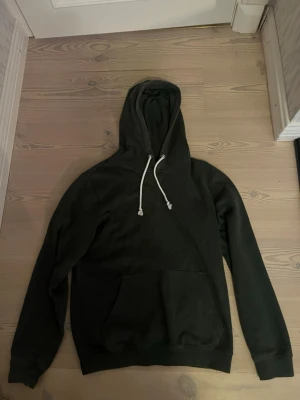 Mörkgrön hoodie från Pier One - Mörkgrön hoodie från Pier One med klassisk känguruficka och vita dragsnören i huvan. Tillverkad i mjukt material som känns skönt mot huden. Perfekt för en avslappnad och stilren look.