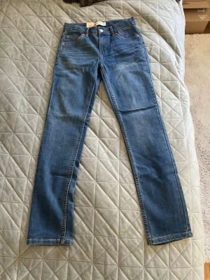 Blå raka jeans från Levi's - Klassiska blå jeans från Levi's med rak passform och normal midja. Jeansen har fem fickor, knappgylf och är tillverkade i slitstark denim. Perfekta för dig som gillar en tidlös och enkel stil.