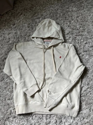 Beige hoodie från Replay - Snygg beige hoodie från Replay med huva och dragsnören. Liten röd logga broderad på bröstet. Tillverkad i mjukt material och har ribbade muddar vid ärmar och nederkant. Perfekt för en avslappnad och stilren look.