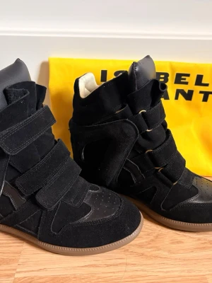 Svarta kilklackar från Isabel Marant - Säljer ett par coola svarta Isabel Marant Beckett sneakers med kilklack. Se bild 5 och 6 för verifiering. De är använda 2 gånger men utan tecken på användning. De är i storlek 39 och orginalpåse medföljer. Klacken är ca 5 cm och de är i mocka. De är perfekta för en stylish look, både till vardags och till fest.                            Kontakta för fler bilder/ frågor💕