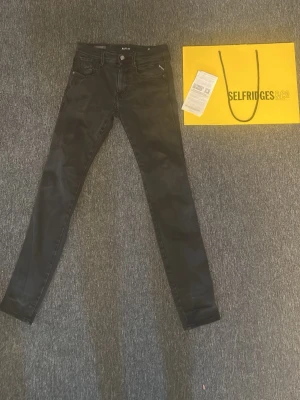 Replay anbass - Säljer ett par svarta slim fit replay anbass hyperflex med klassisk femficksdesign. Jeansen har normal midja och smala ben, perfekta till en trendig vardagslook. Passar dig som gillar stilrena och enkla plagg. Tyvärr har det gått hål på den lilla fickan på vänster sida men det syns inte vid användning förutom att de är lite slitna där. Köpte av mig på selfridges i London.
