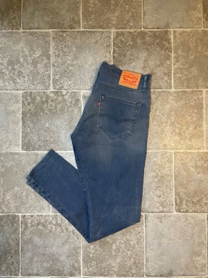 Blå Levi's 520 slim jeans - Snygga blå Levi's 520 slim jeans med klassisk femficksdesign och läderpatch bak i midjan. Jeansen har en smal passform och subtila slitningar framtill för en avslappnad look. Perfekta för dig som gillar tidlös stil och vill ha ett par jeans som funkar till det mesta.