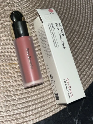 Rare Beauty Soft Pinch Dewy Liquid Blush - Flytande rouge från Rare Beauty i nyansen Hope, en mjuk rosa ton. Kommer i en frostad glasflaska med silvrig och guldfärgad kork. Formulan är lätt och ger en naturlig, daggig finish. Förpackningen innehåller 7,5 ml.
